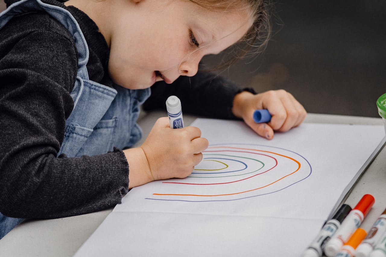 Little girl drawing rainbow on paper